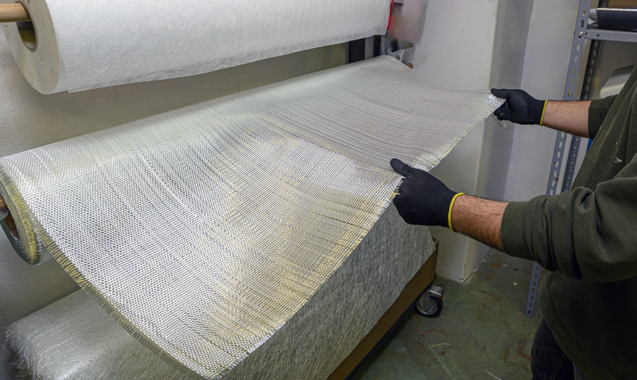 Worker handling a woven fiberglass fabric roll on a coating machine